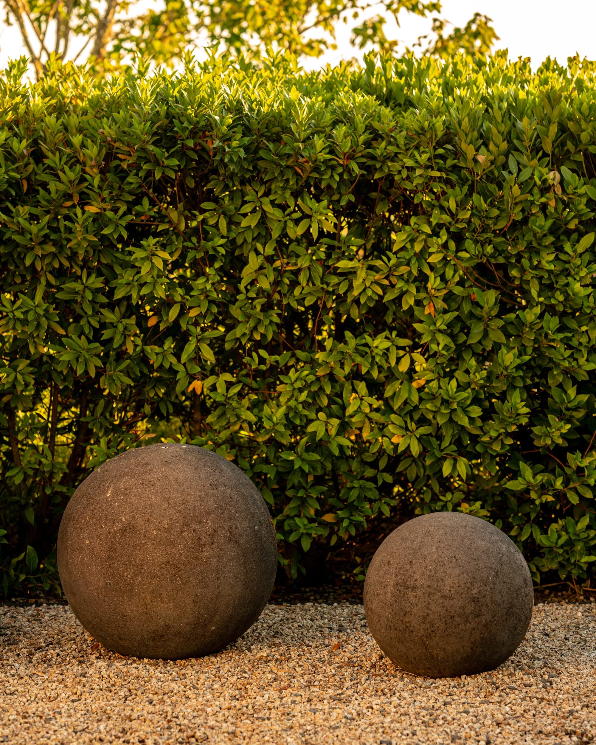 Two weathered stone spheres set against a clipped green hedge