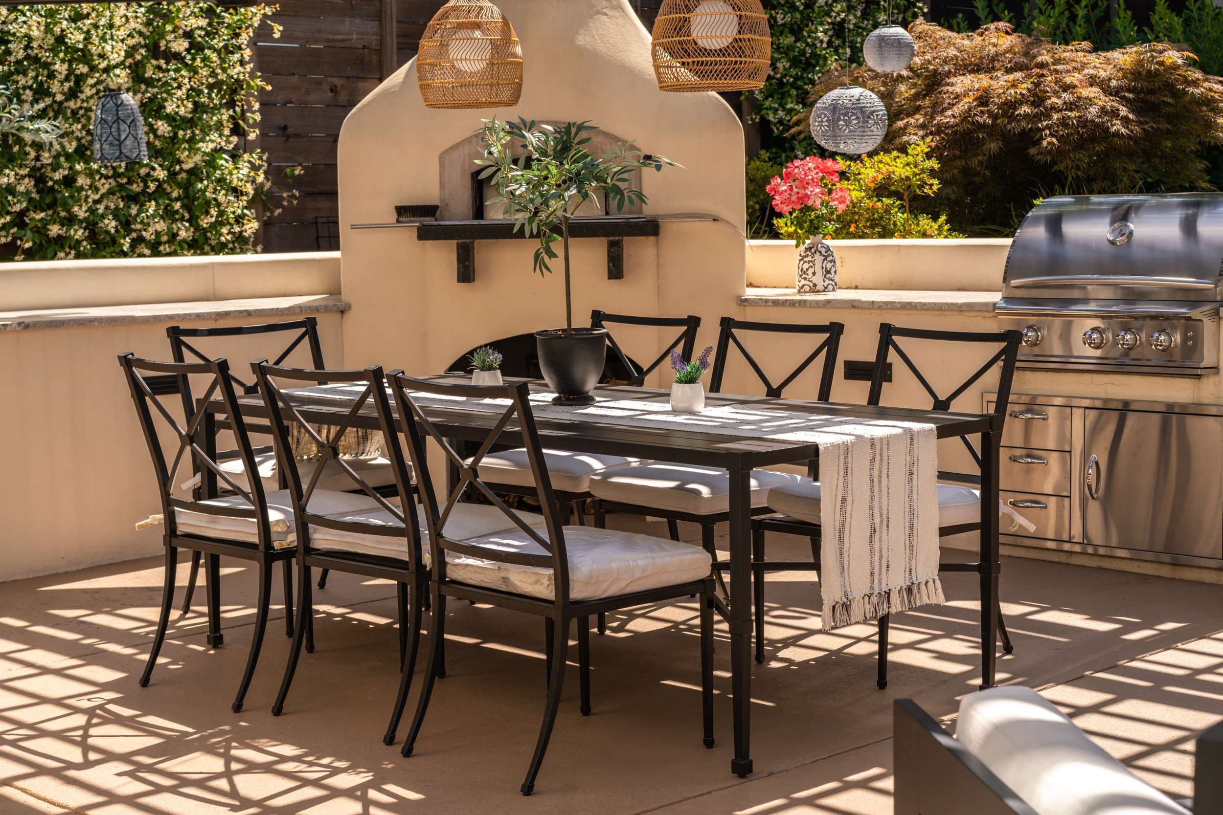 Sunlit garden dining terrace with an outdoor fireplace and layered planting